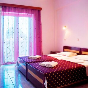 A hotel room with two beds, a large window with curtains, and a nightstand with a lamp.