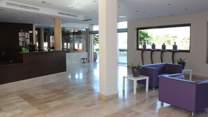 Un vestíbulo moderno con mostrador de recepción, zona de estar y ventanas amplias que ofrecen vistas al exterior.