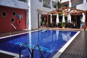 A swimming pool with a wooden deck, a covered seating area, and a lifebuoy on the wall. - Hotel Puerto Mar (Peniscola)