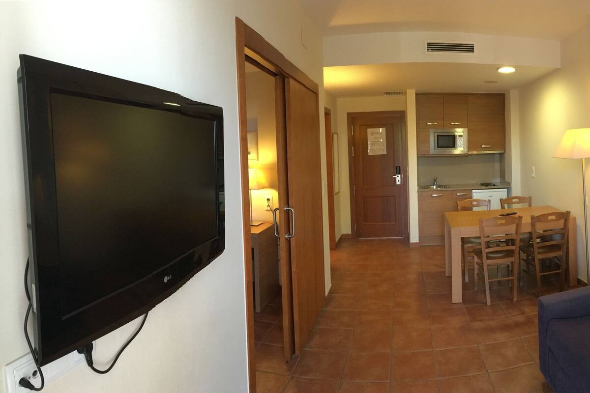 A compact living space with a flat-screen TV, a dining area with a table and chairs, and a sofa.