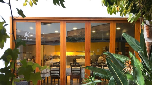 Un restaurante con cerramientos de vidrio, estructura de madera y plantas de interior.