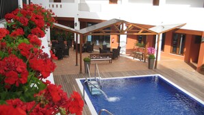 Un área de piscina en la azotea, con piscina, asientos exteriores y flores rojas.