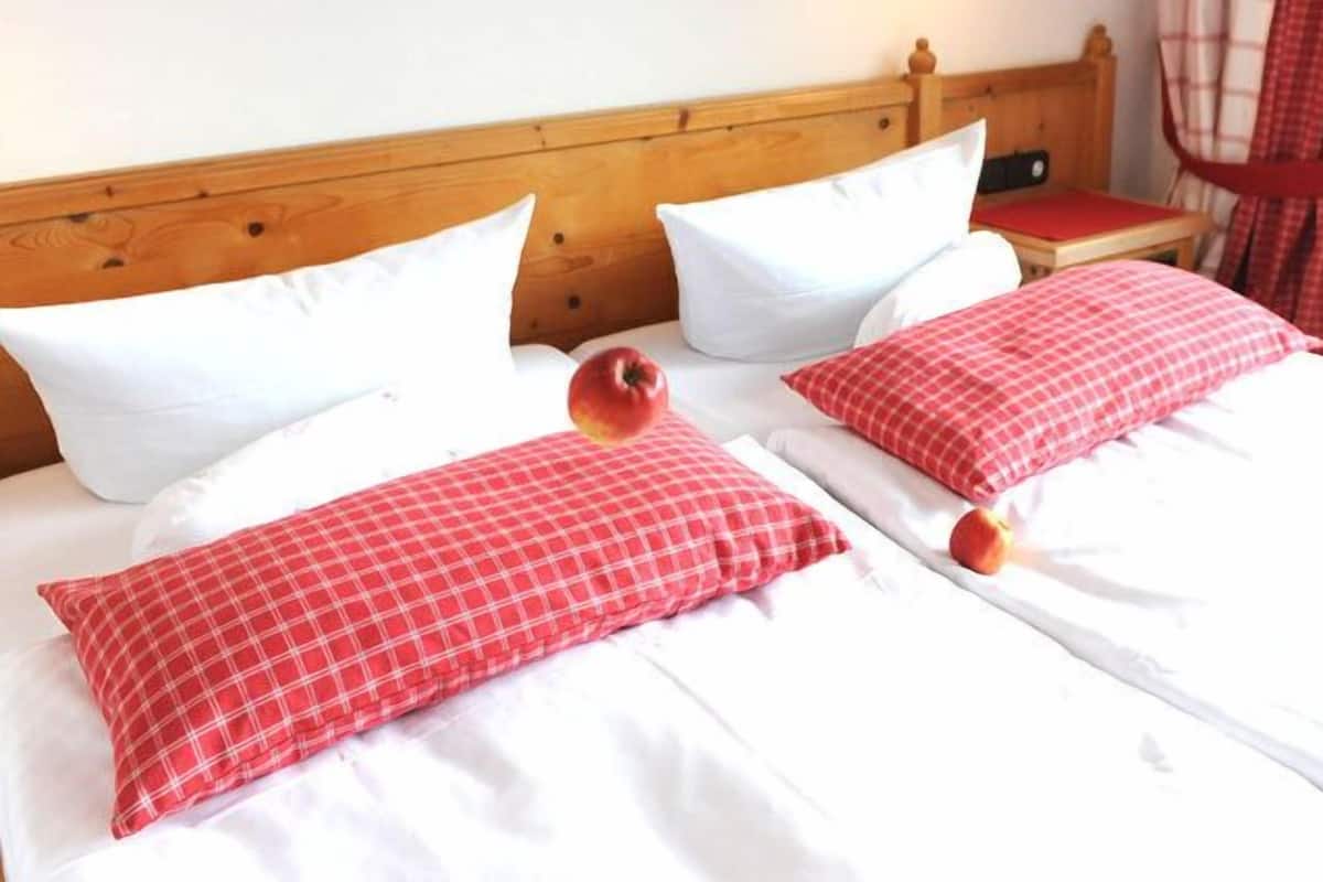 A double bed with white and red checkered bedding, a wooden headboard, and a small bedside table with a red cushion.