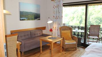 Une pièce avec un plancher en bois, un canapé, un fauteuil, une table avec une lampe et un tableau accroché au mur.