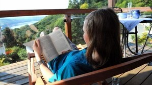 A person reading a book on a wooden deck with a table and chairs in the background. - Hotel Garni Belvedere, das BIO Hotel & SuiteHotel am Ederse (Waldeck)
