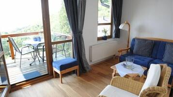 Une pièce confortable avec un canapé, un fauteuil, une petite table et une fenêtre avec des rideaux.