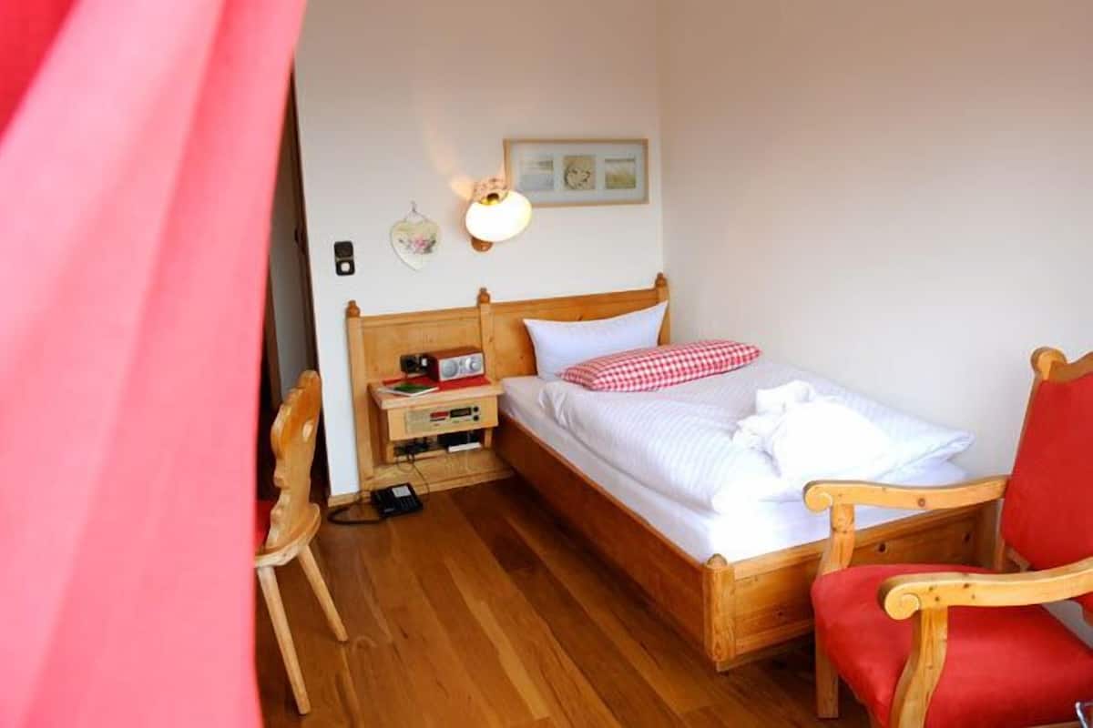 A wooden bed with white bedding, a nightstand with a lamp, and a red chair.
