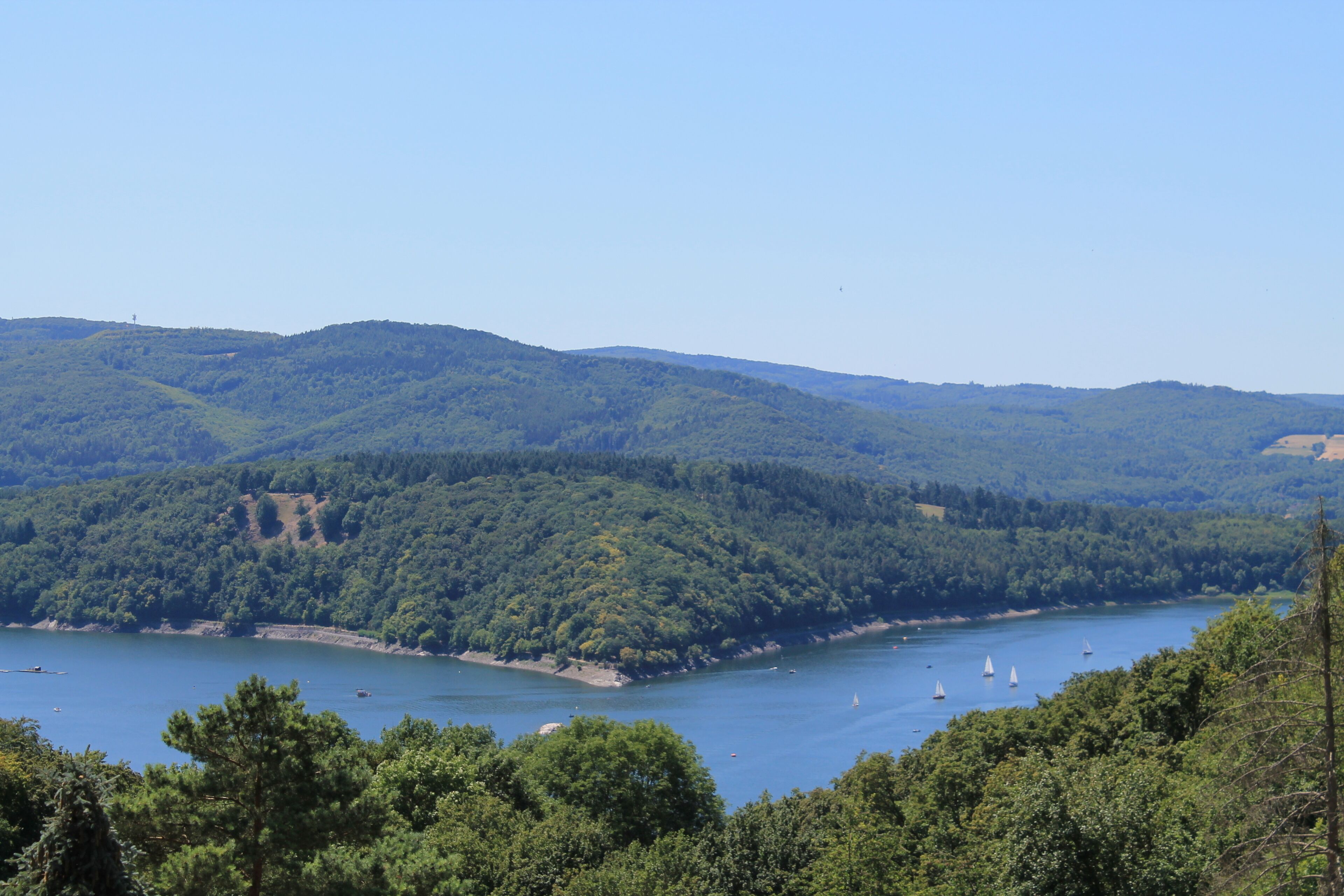 A lake surrounded by forested hills with boats and sailboats.