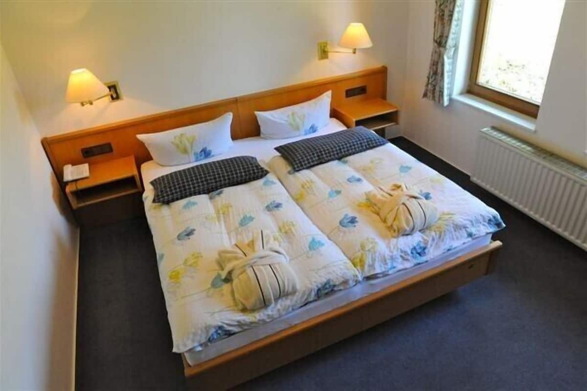 A double bed with floral bedding, two bedside tables with lamps, and a window with curtains.