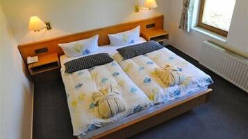 Una cama doble con ropa de cama floral, dos mesitas de noche con lámparas y una ventana con cortinas.