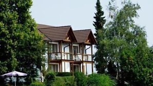 A two-story wooden building with a tiled roof, surrounded by lush greenery and trees. - Hotel Garni Belvedere, das BIO Hotel & SuiteHotel am Ederse (Waldeck)