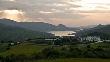 A rural landscape with a lake, rolling hills, and a white building with multiple windows and a red roof.