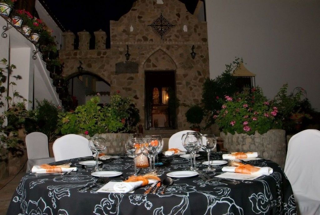Un espacio de comedor al aire libre con paredes de piedra, sillas blancas y una mesa dispuesta con platos, vasos y un centro de mesa.