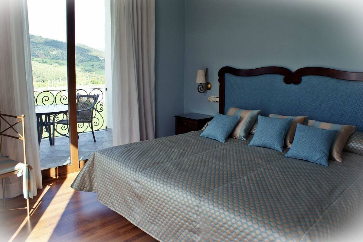 A bedroom with a bed, a nightstand, a lamp, and a view of a balcony with a chair.