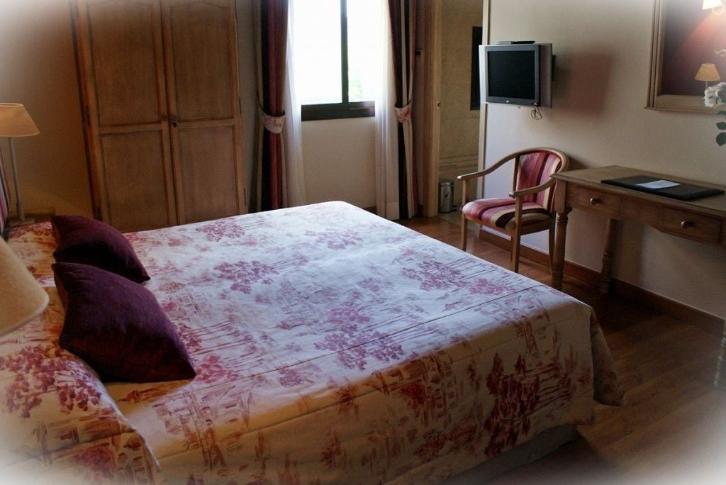 A hotel room with a bed, a desk, a chair, a television, and a wardrobe.