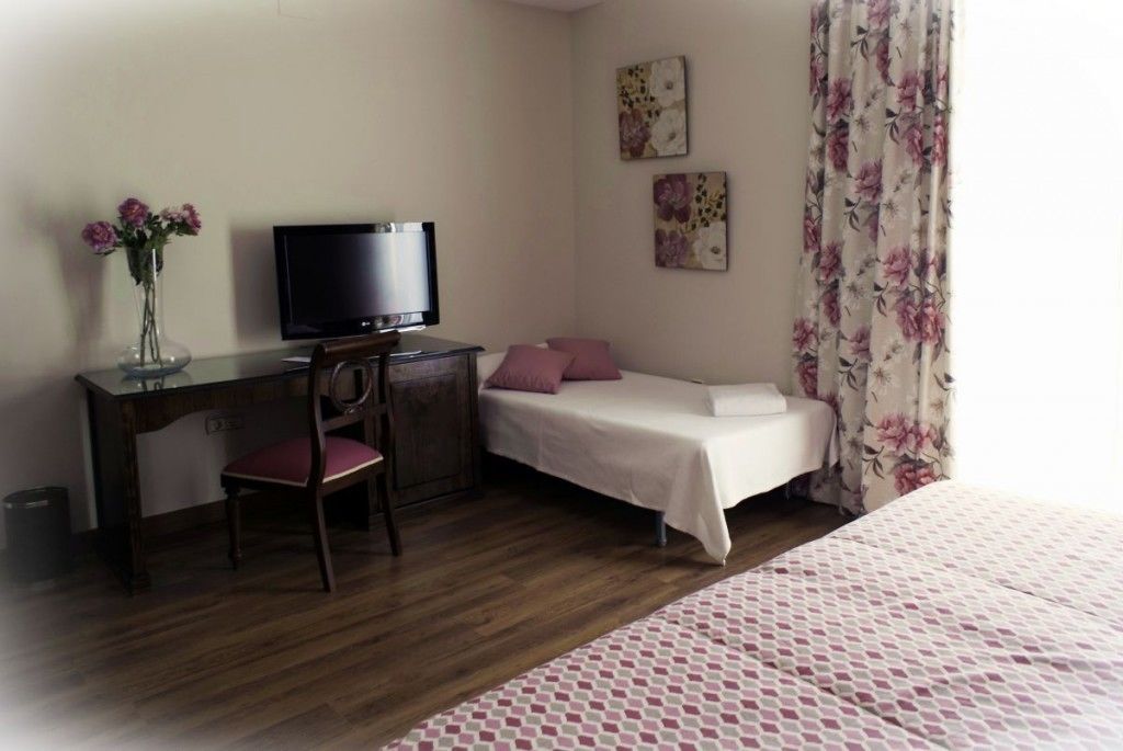 Un dormitorio con cama, escritorio, silla, televisor y una mesita.