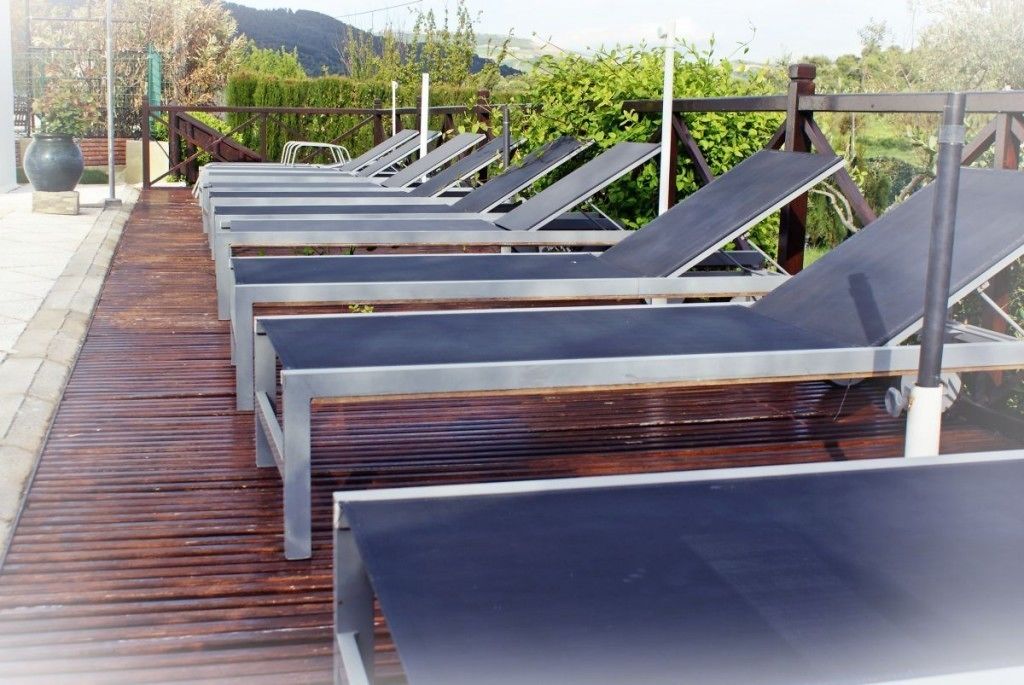 Fila de tumbonas en una terraza de madera con vistas a zonas verdes y colinas al fondo.