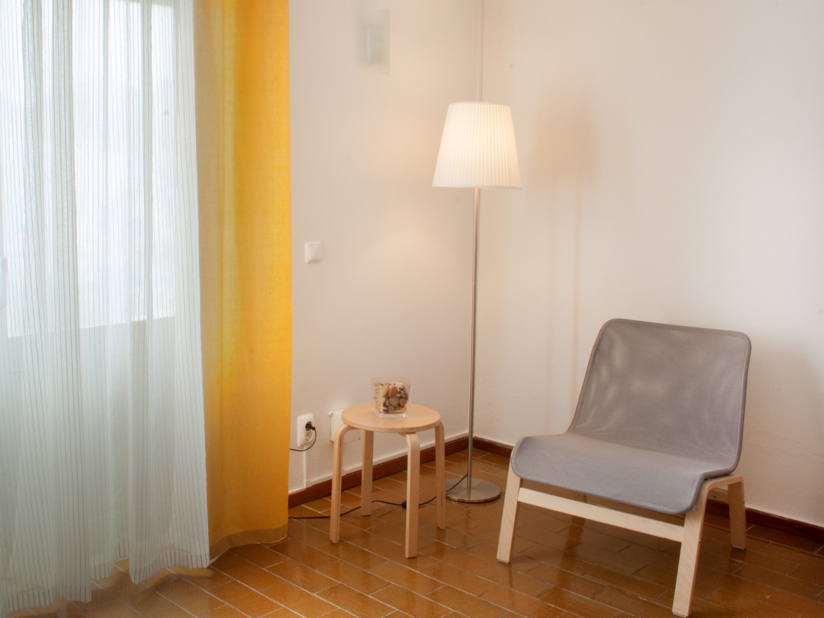 A room with a chair, a small table, a lamp, and a curtain.
