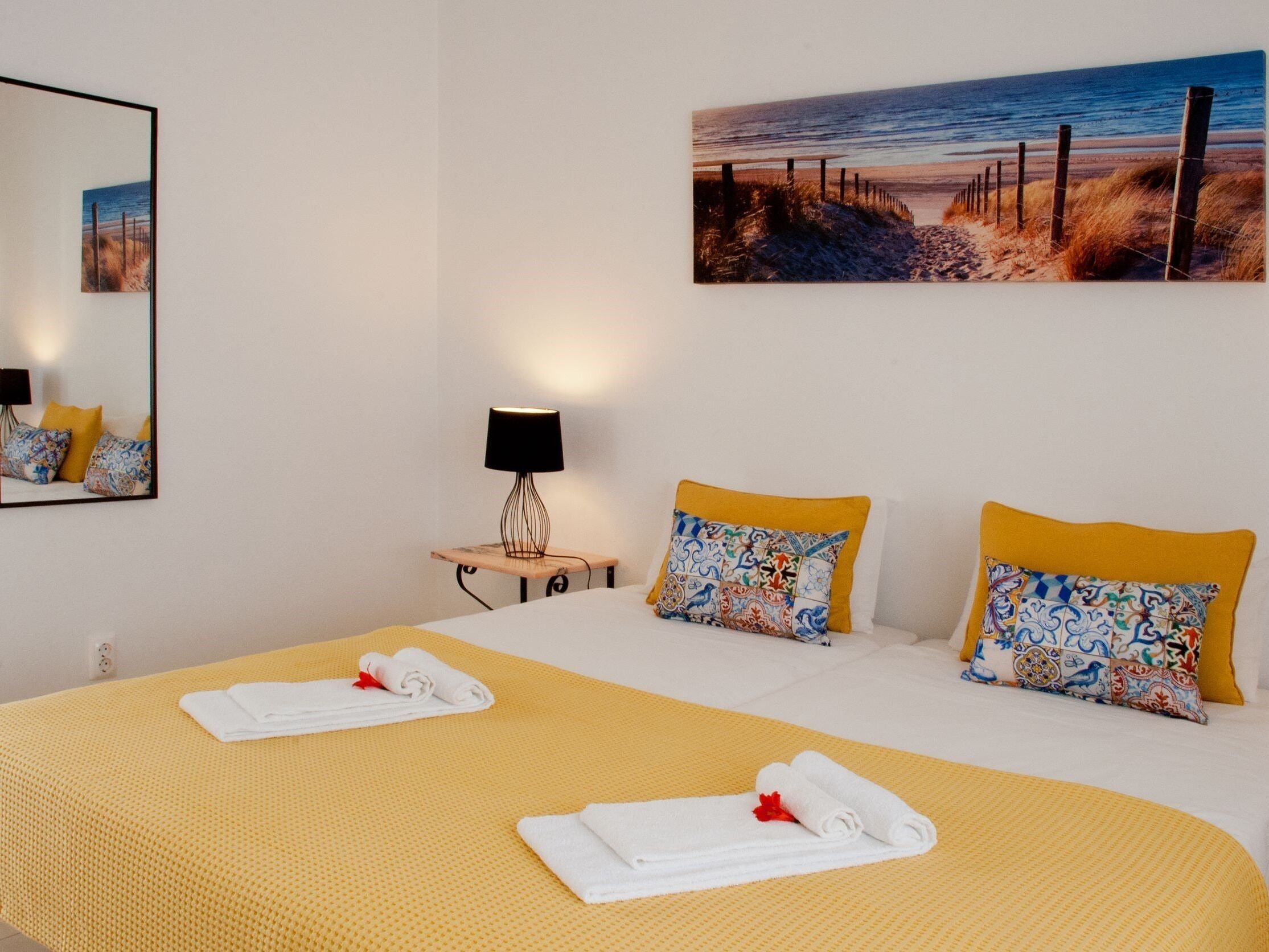 A hotel room with a bed, a bedside table with a lamp, and a painting of a beach scene.