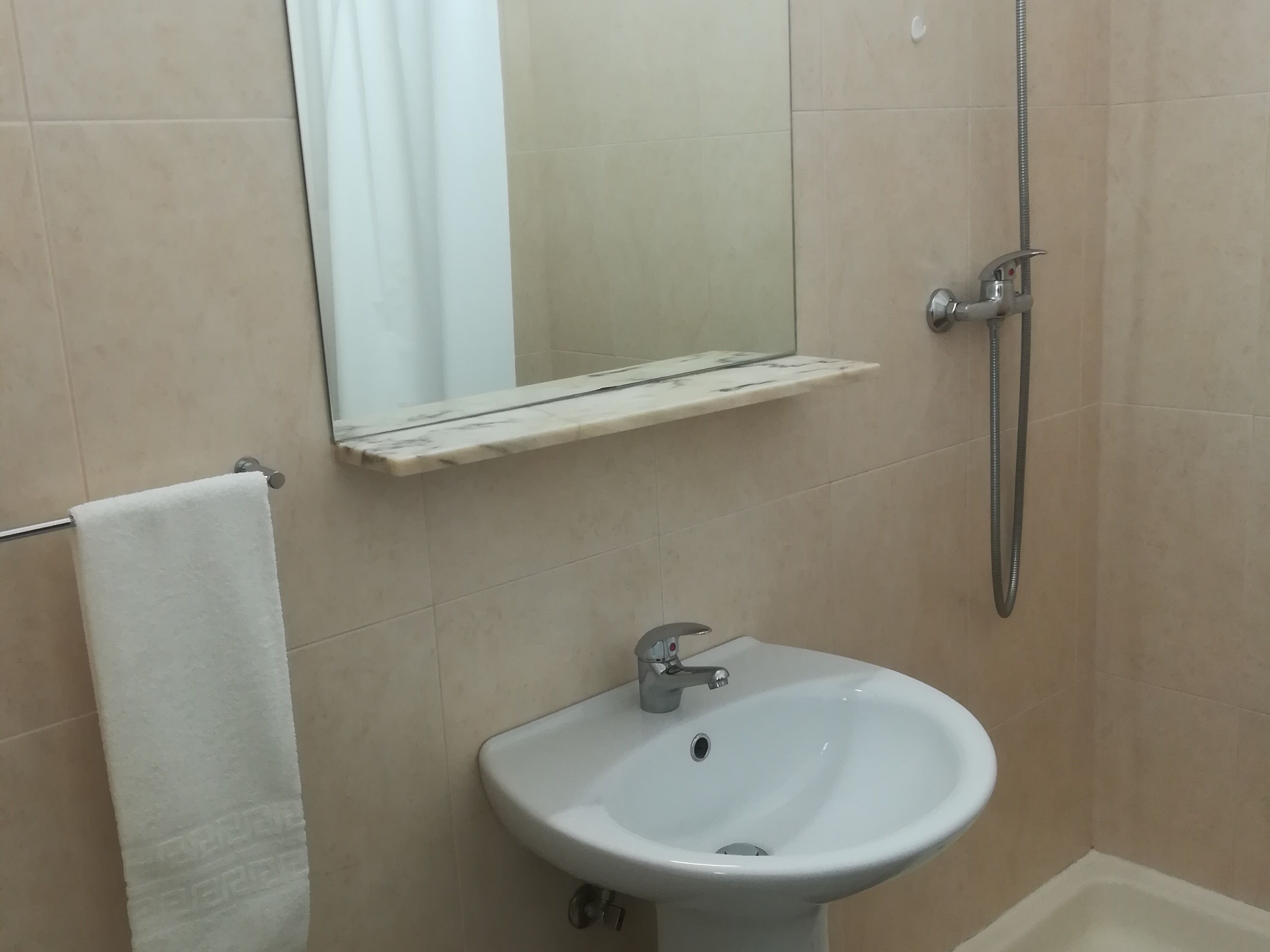 Een badkamer met een witte wastafel, een spiegel en een douche.