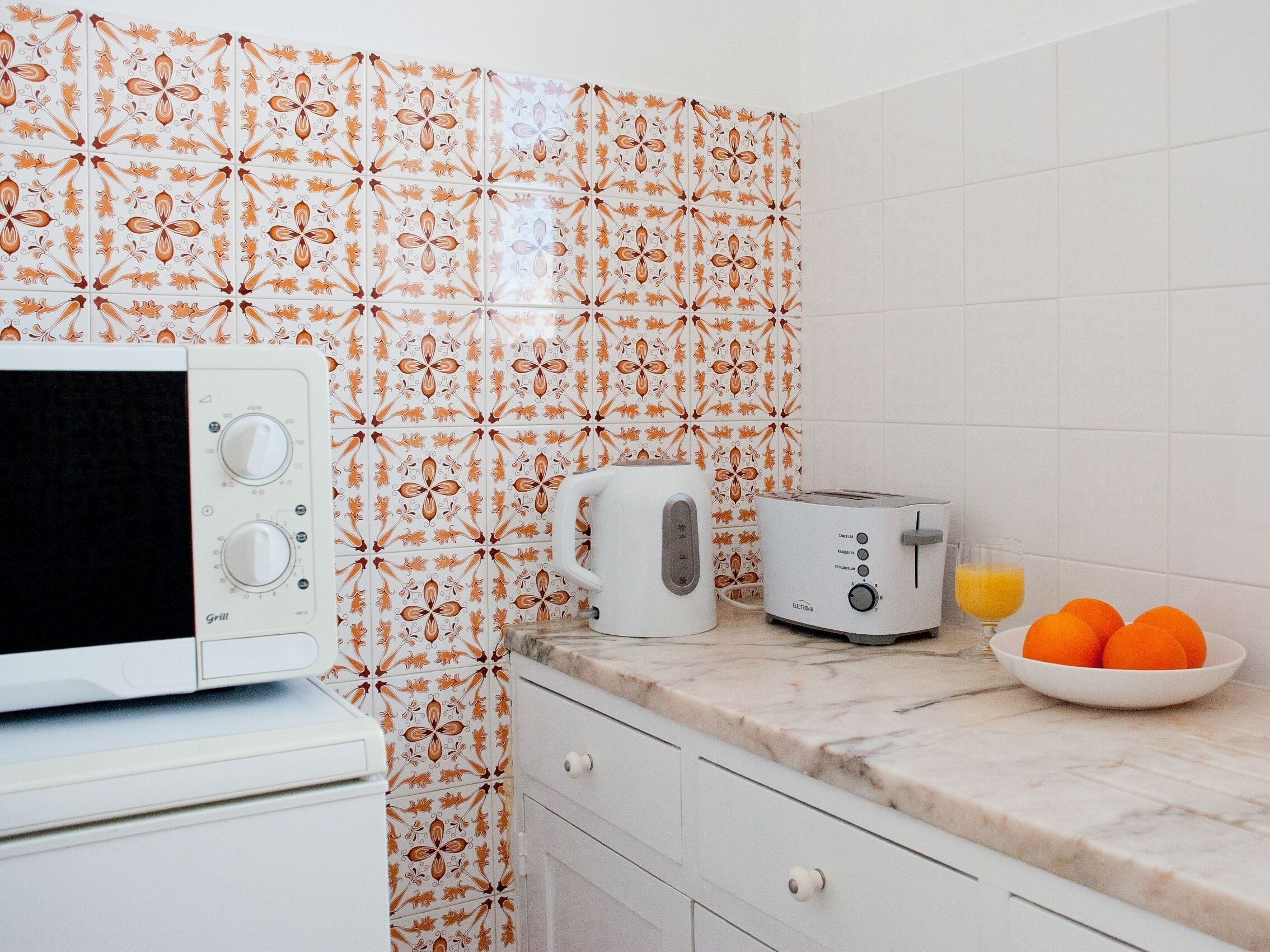 A kitchen with a microwave, toaster, and a bowl of oranges on the counter.