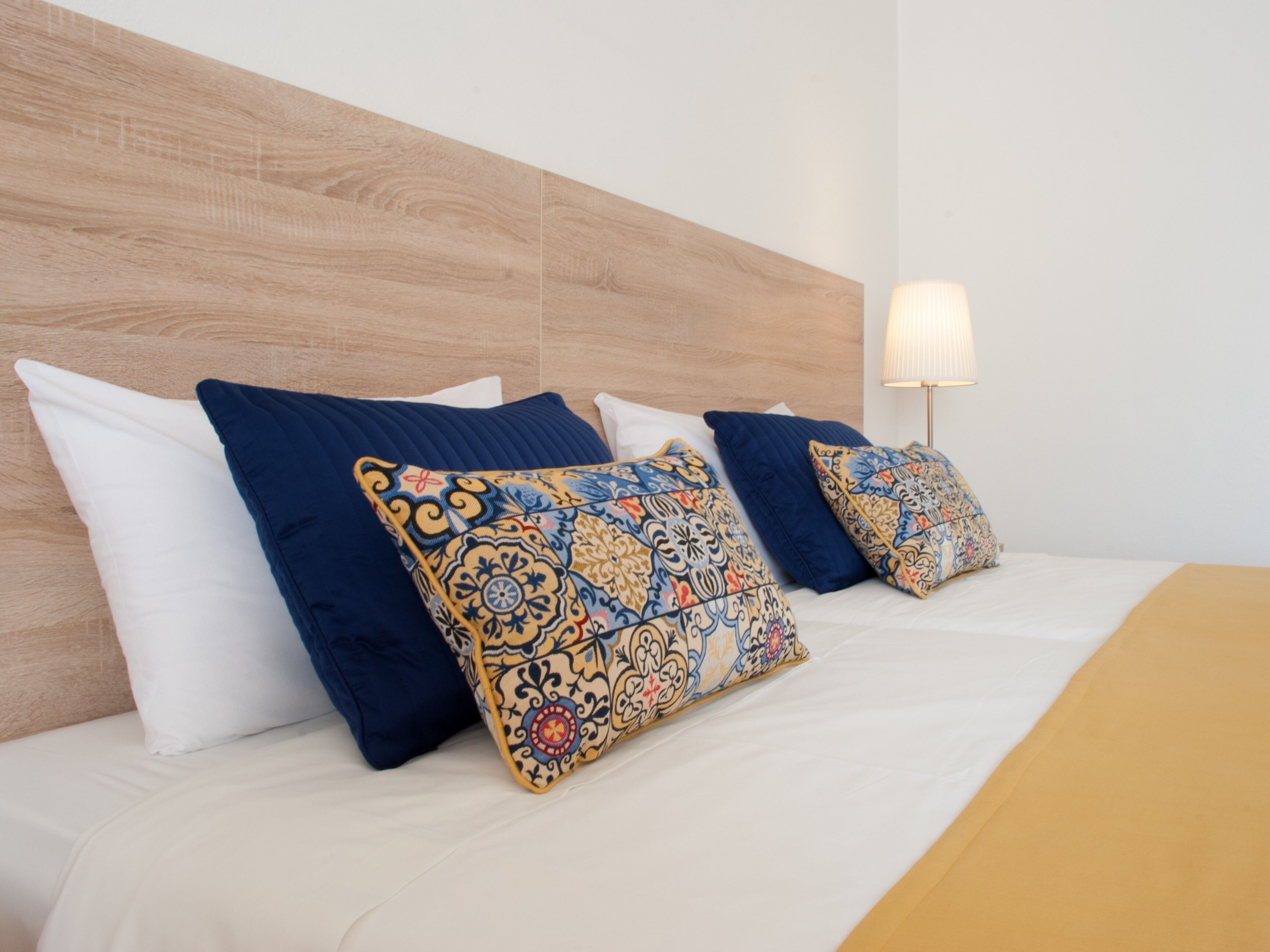 Een net opgemaakt bed met gestreepte kussens en een houten hoofdeinde.