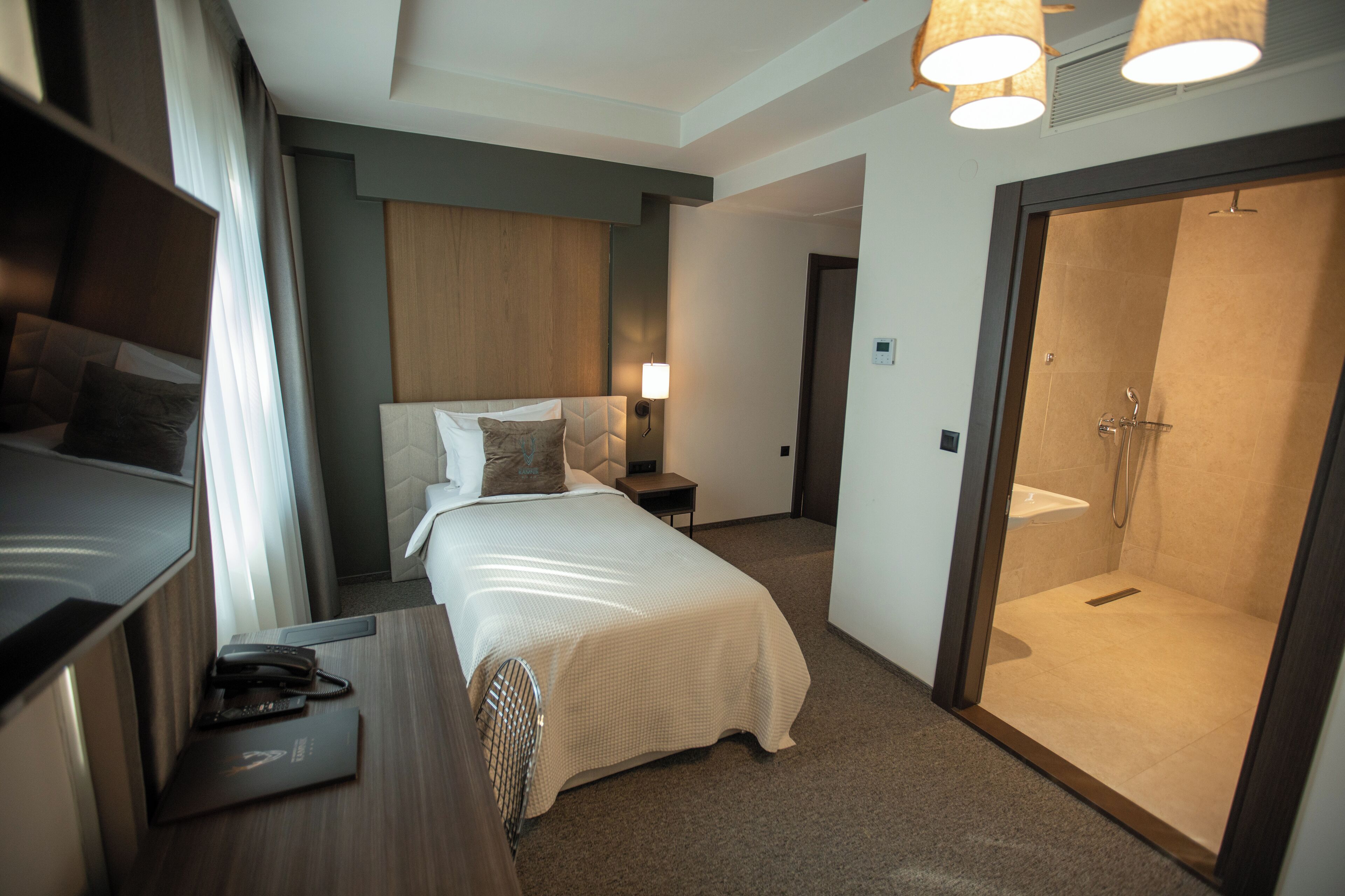Quarto de hotel com cama, mesa de cabeceira, luminária e área de banho.