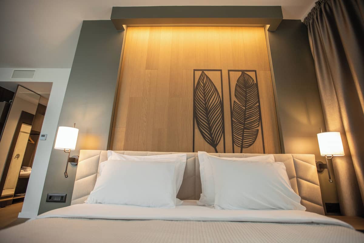A hotel room with a large bed, two bedside lamps, and a wooden headboard with leaf designs.