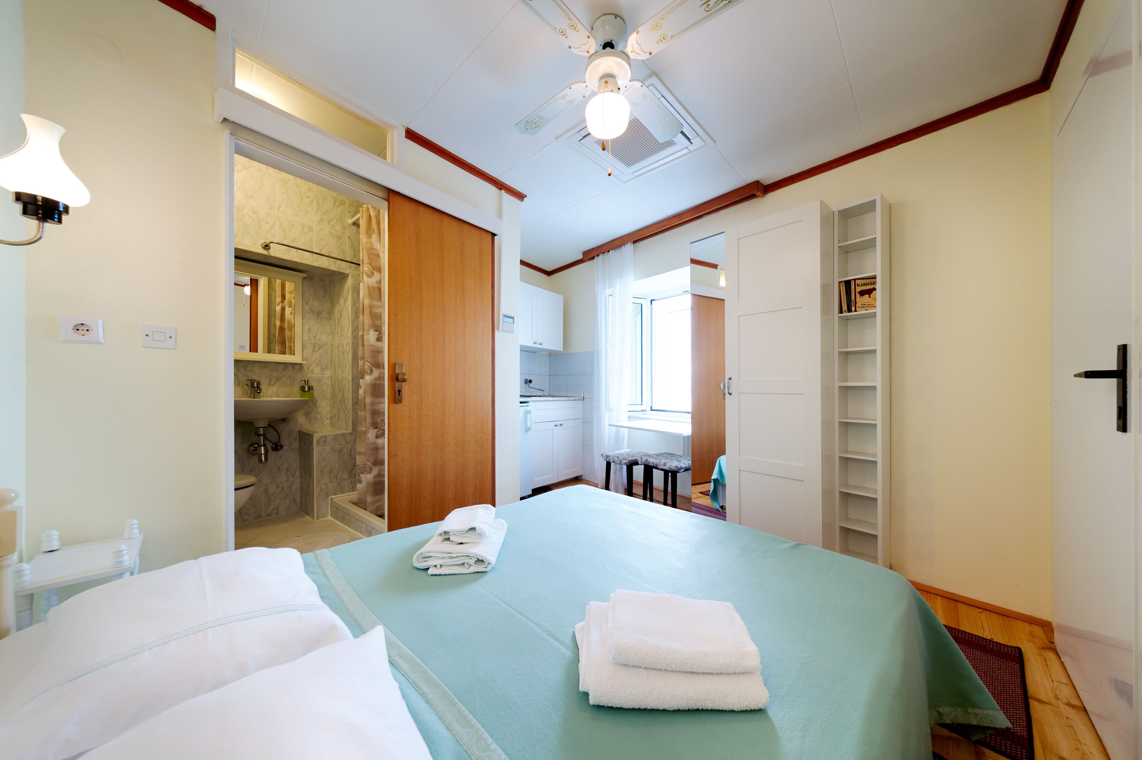 A hotel room with a bed, a bathroom, a small kitchen, and a bookshelf.