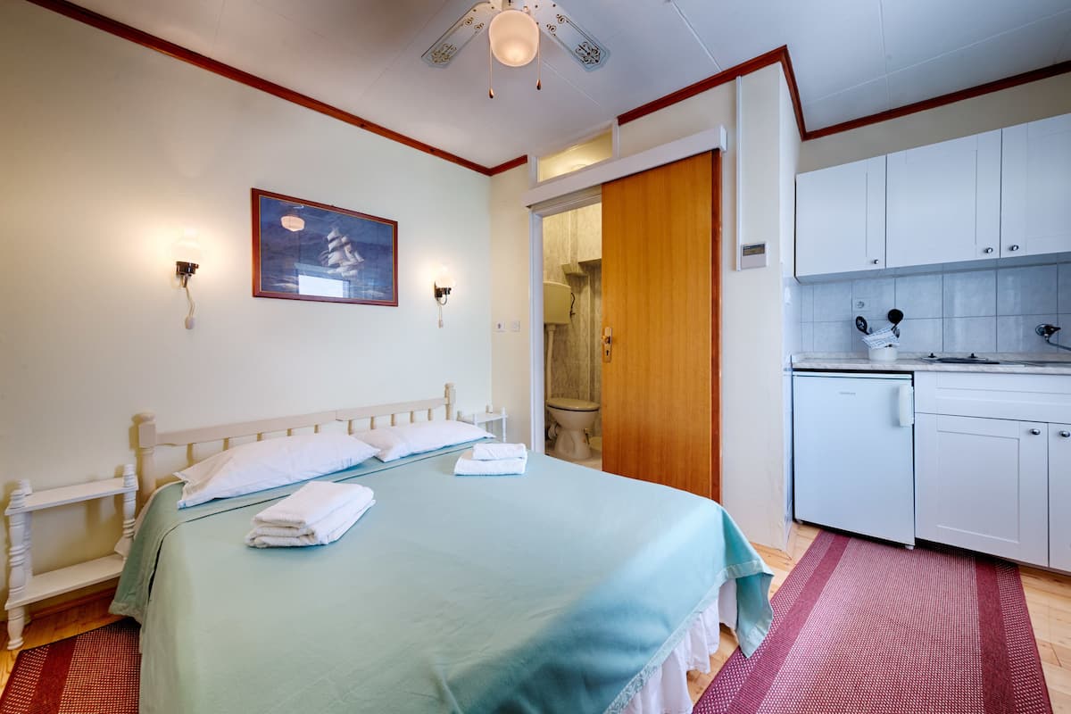 A hotel room with a bed, a wooden door, a kitchenette, and a bathroom.