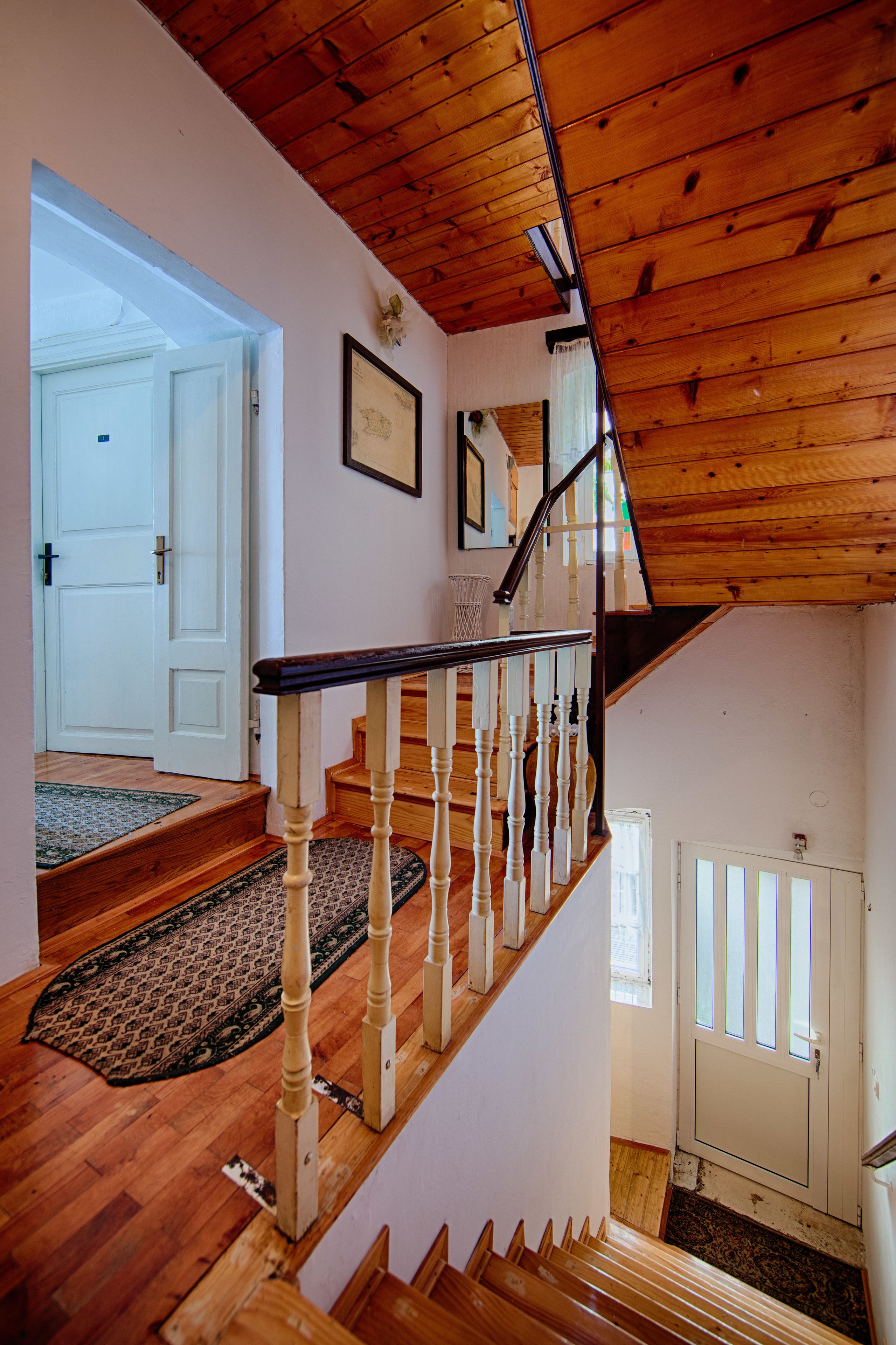 Eine Holztreppe mit weißen Balustraden, ein gemustertes Teppich an der Basis und eine Tür, die in einen anderen Raum führt.