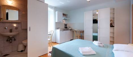 Un dormitorio con cama, ventilador de techo, baño con lavamanos y espejo.