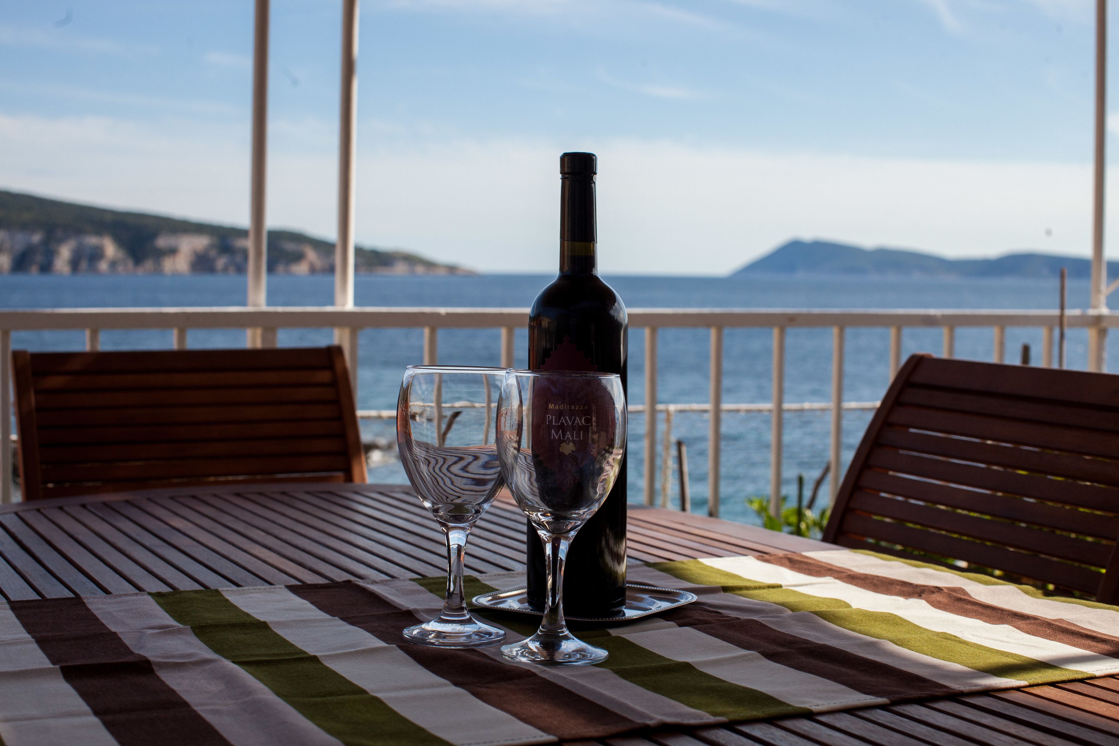 A table with two wine glasses and a bottle on a striped tablecloth, overlooking a scenic coastal view.