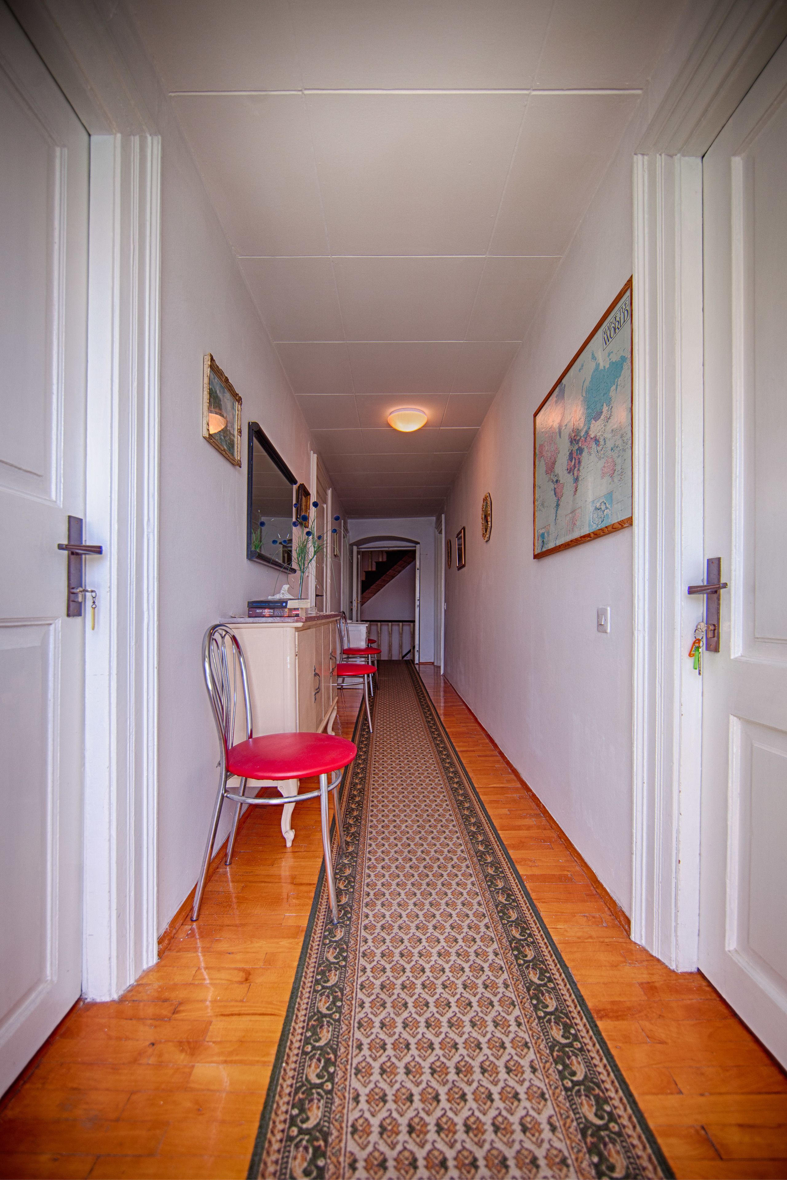 A hallway with wooden flooring, a patterned rug, and a red chair.