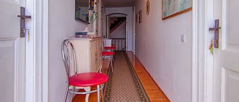 A hallway with wooden flooring, a patterned rug, and a red chair.