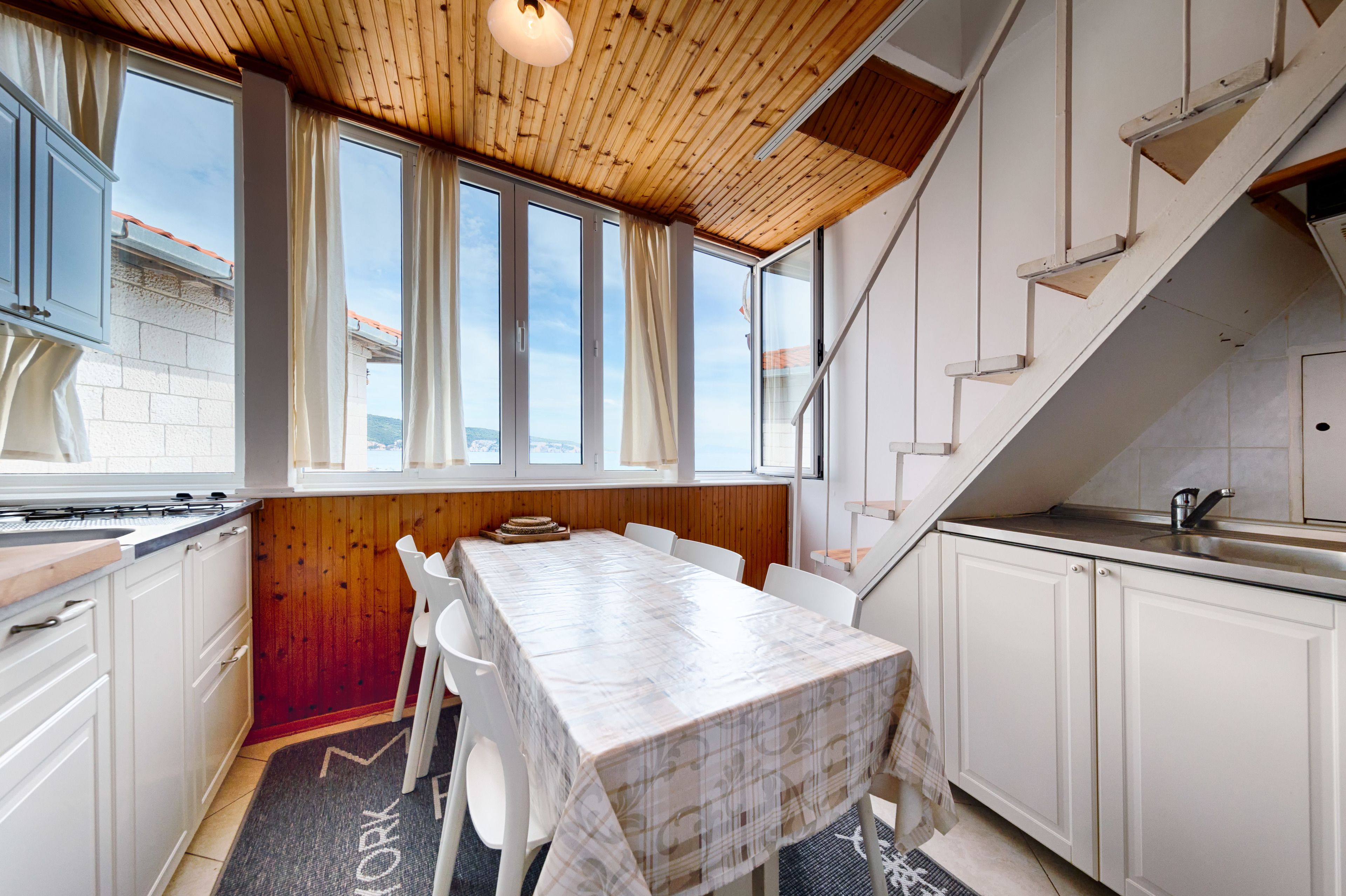 A compact kitchen with white cabinets, a wooden ceiling, and a dining area with a table and chairs.