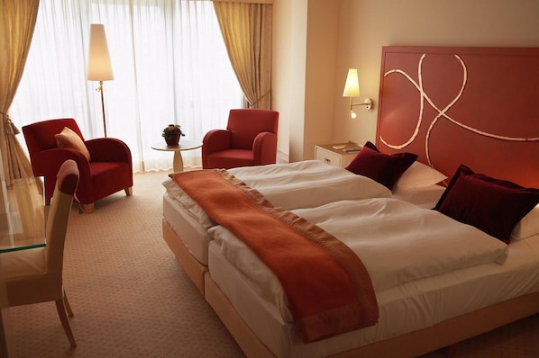 A hotel room with two beds, a sitting area with a table and chairs, and a large window with curtains.
