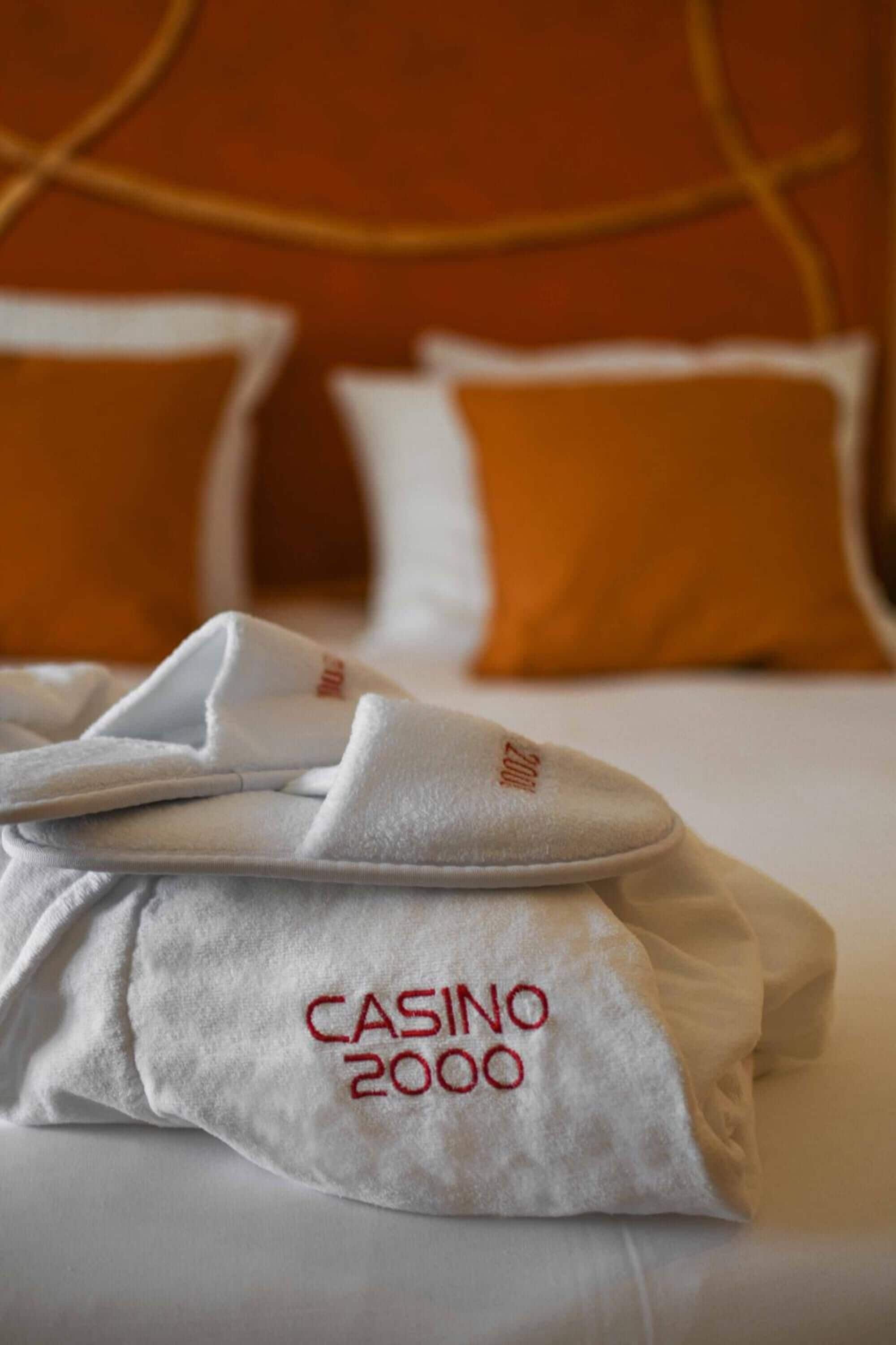 Una cama bien hecha con una toalla blanca y una almohada blanca con el bordado 'CASINO 2000'.