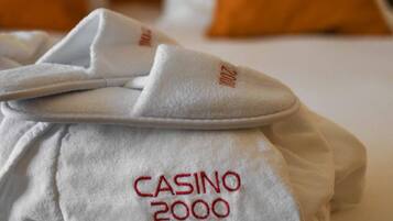 Una cama bien hecha con una toalla blanca y una almohada blanca con el bordado 'CASINO 2000'.