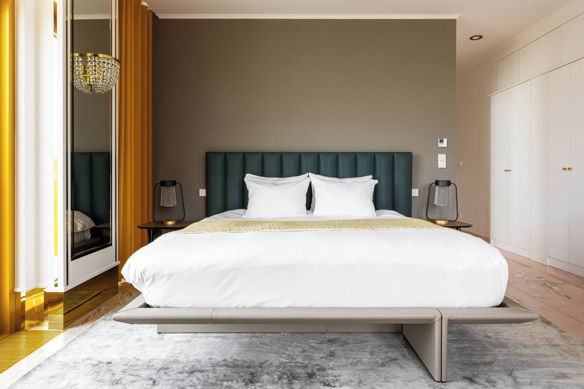 A modern bedroom with a large bed, bedside lamps, a chandelier, and a wardrobe.