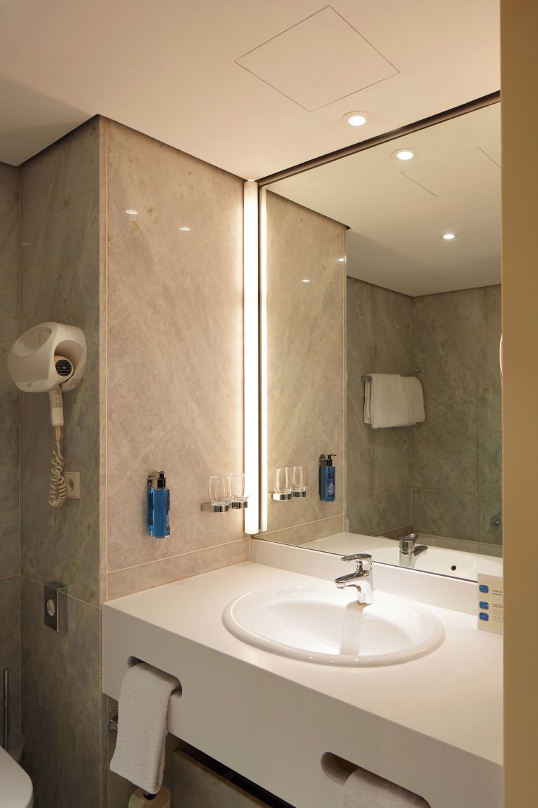 A modern bathroom with a large mirror, a sink, and a hairdryer on the wall.