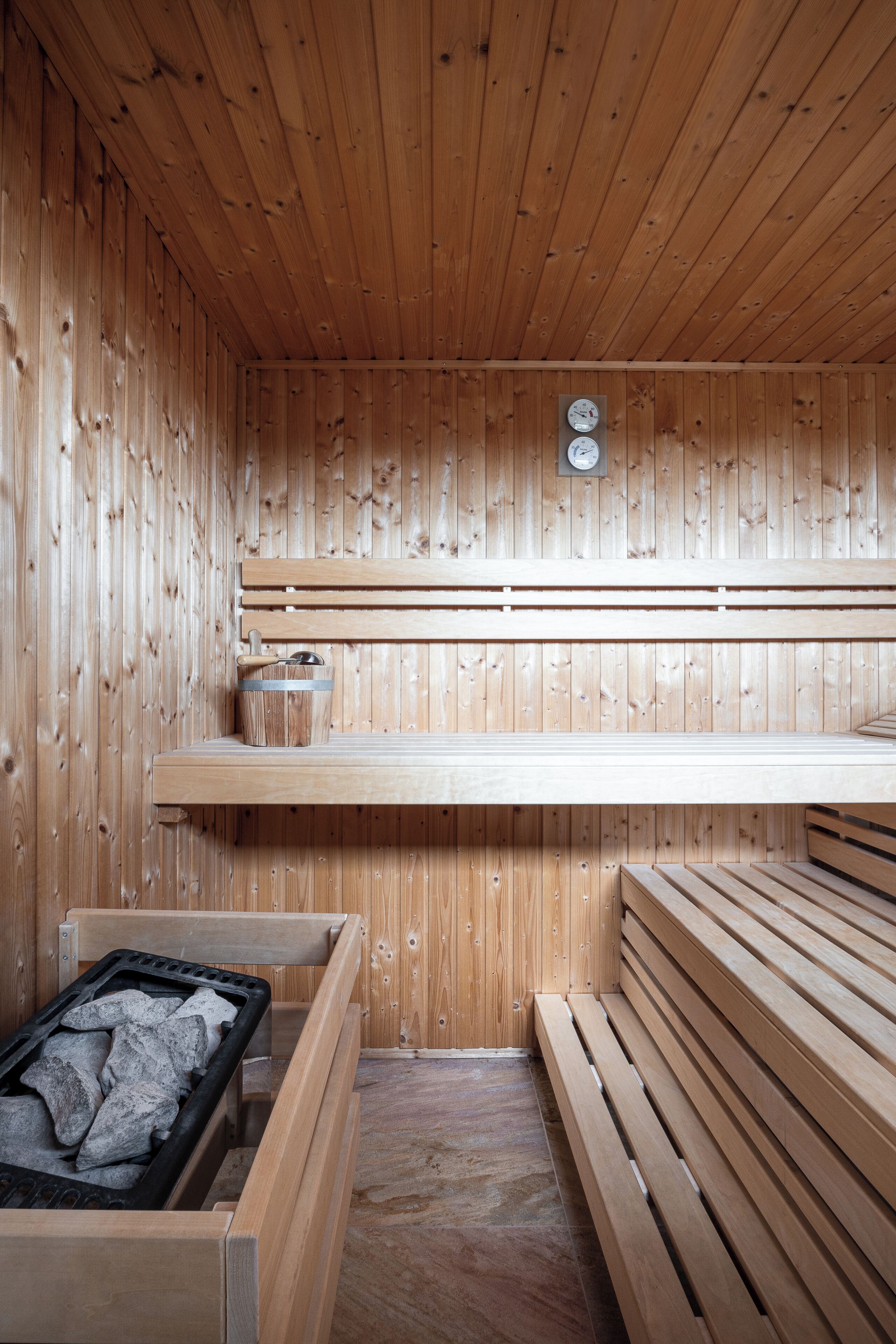A wooden sauna with benches, a bench with a heater, and a wooden wall with a clock.