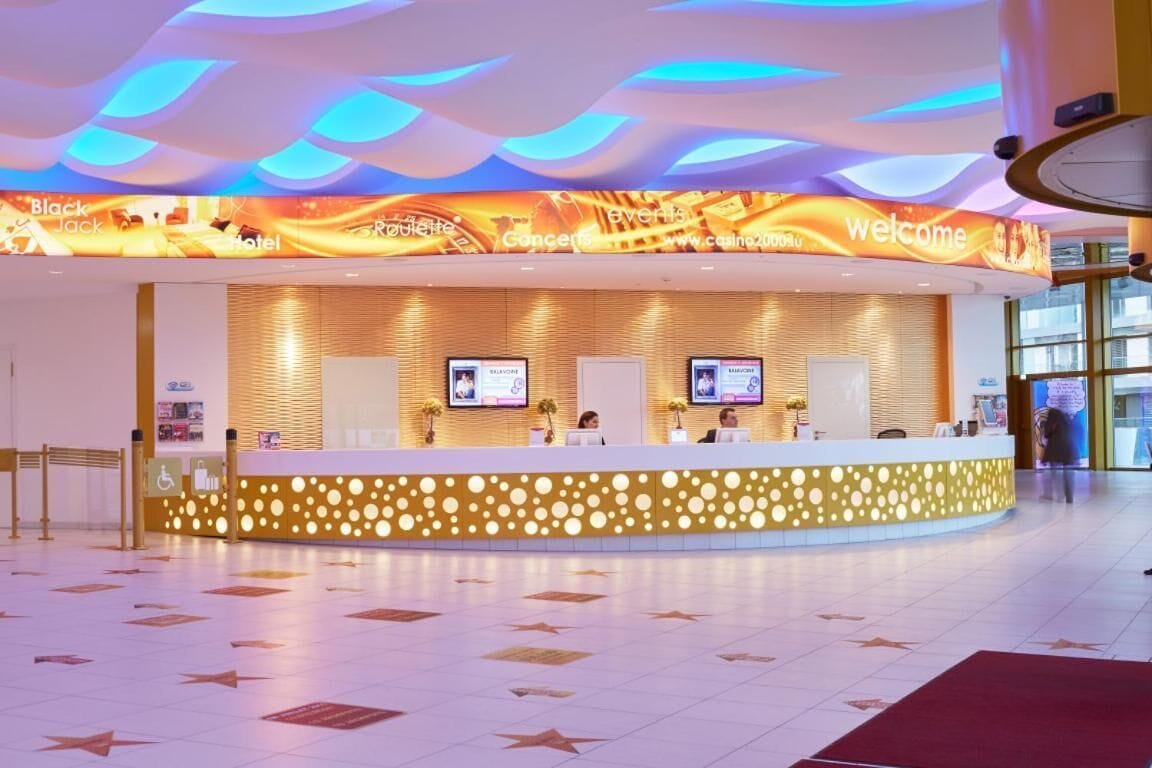 Zona de recepción de hotel con diseño moderno, que incluye un mostrador curvo, pantallas digitales y un suelo con diseño.