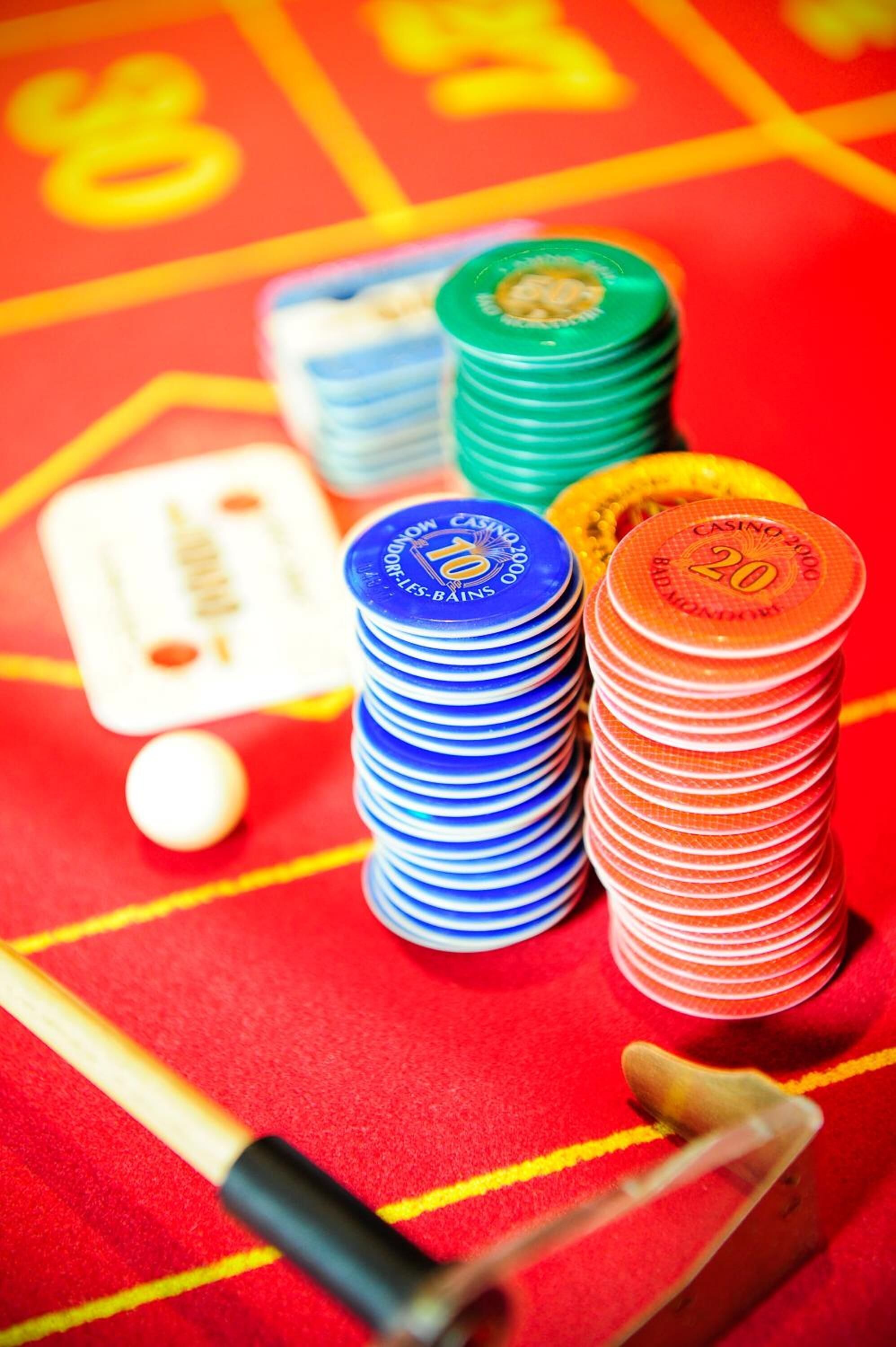 Montones de fichas de póker en azul, verde y naranja, una ficha de póker blanca y una mesa de juego con superficie de fieltro rojo.