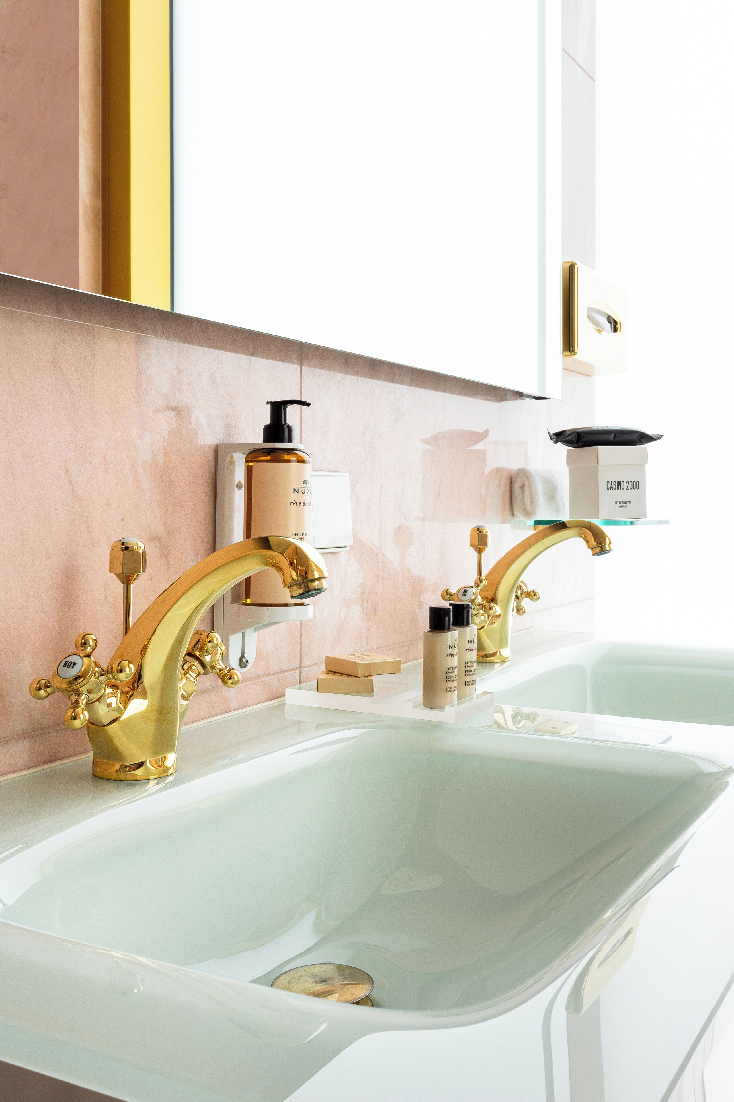 Ein Badezimmer mit zwei goldenen Wasserhähnen, einem weißen Waschbecken und einem Spiegel darüber.