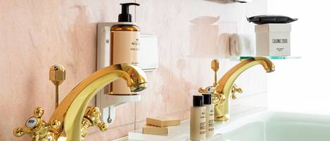 Ein Badezimmer mit zwei goldenen Wasserhähnen, einem weißen Waschbecken und einem Spiegel darüber.