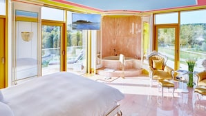 Un dormitorio espacioso con una cama grande, una zona de estar con un sillón dorado y vistas al exterior.