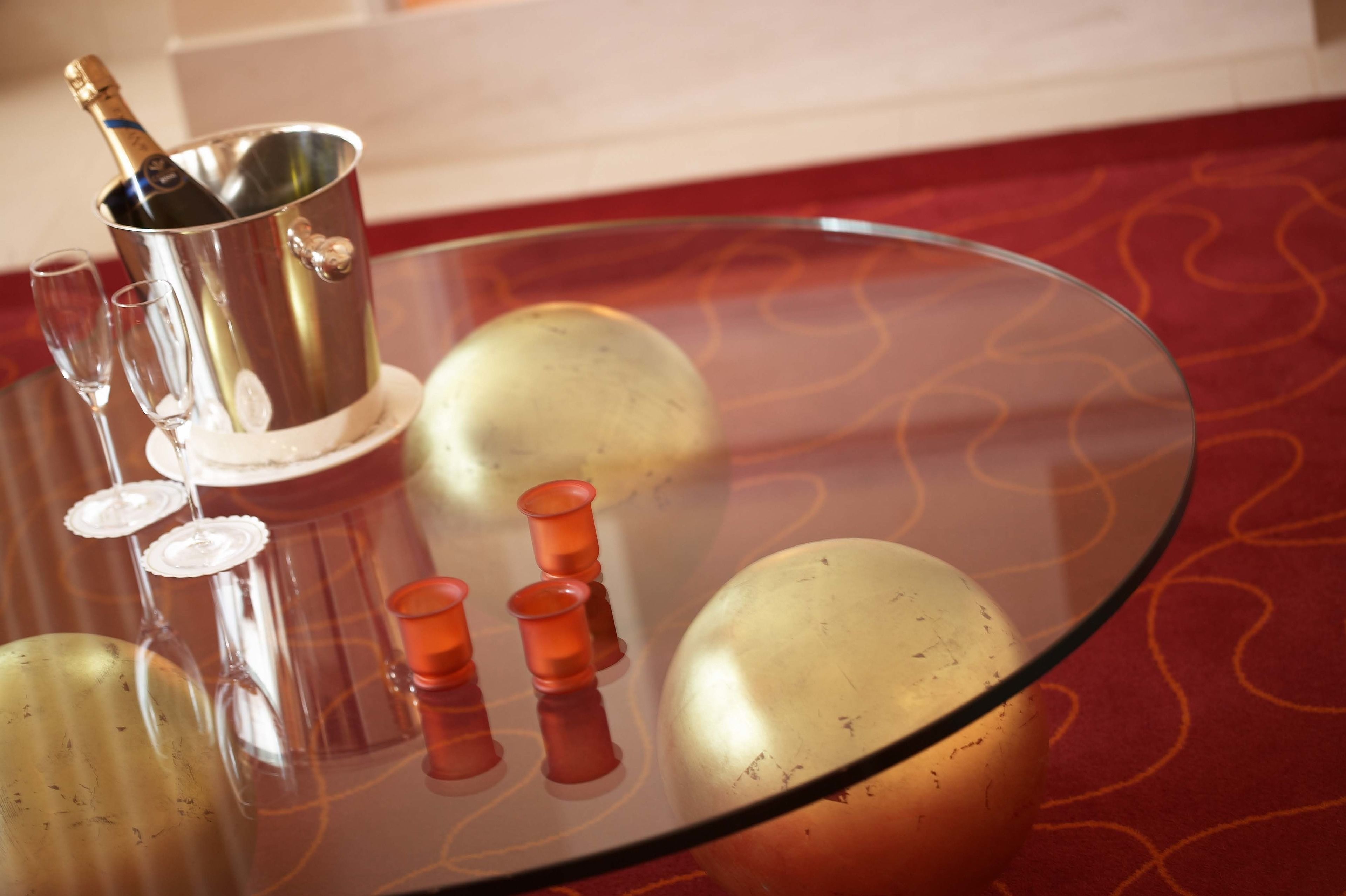 Uma mesa de vidro com uma garrafa de champanhe, três taças de vinho e quatro pequenos copos para shots alaranjados.