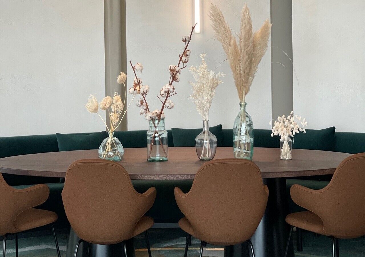 Uma mesa redonda com seis cadeiras marrons, em volta de um sofá verde.