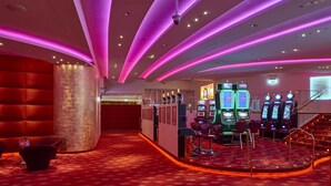 Zona de casino con máquinas tragamonedas, un bar y suelo cubierto de alfombra roja.